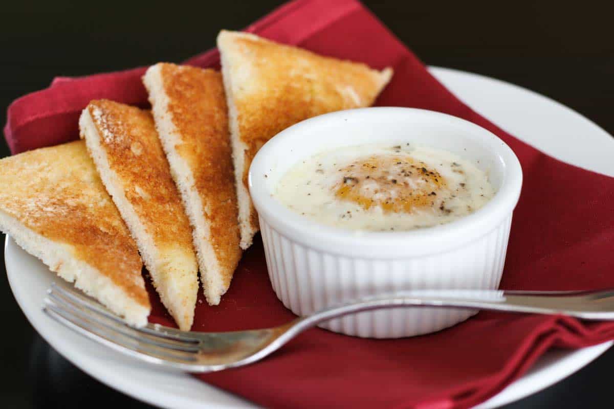 Single ramekin with baked egg over creamed spinach served with toast triangles.