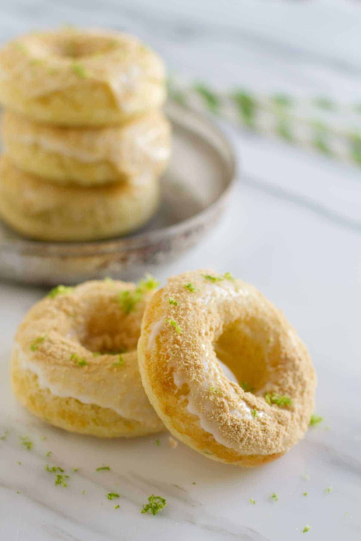 two baked key lime pie donuts in front of a stack of donuts