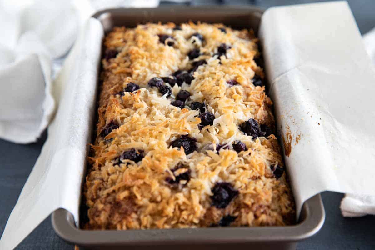 loaf of blueberry banana bread in a baking pan with parchment paper.