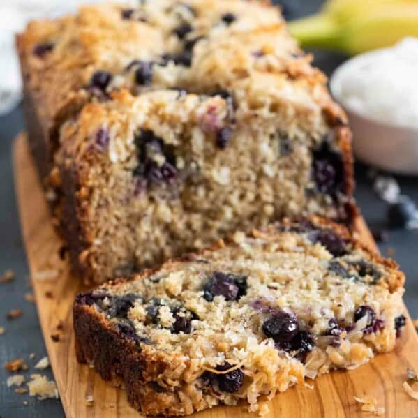 loaf of blueberry banana bread with a slice of bread on a cutting board.