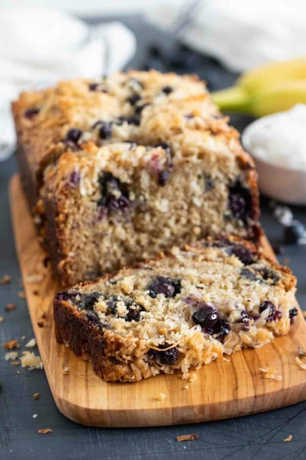 loaf of blueberry banana bread with a slice of bread on a cutting board.