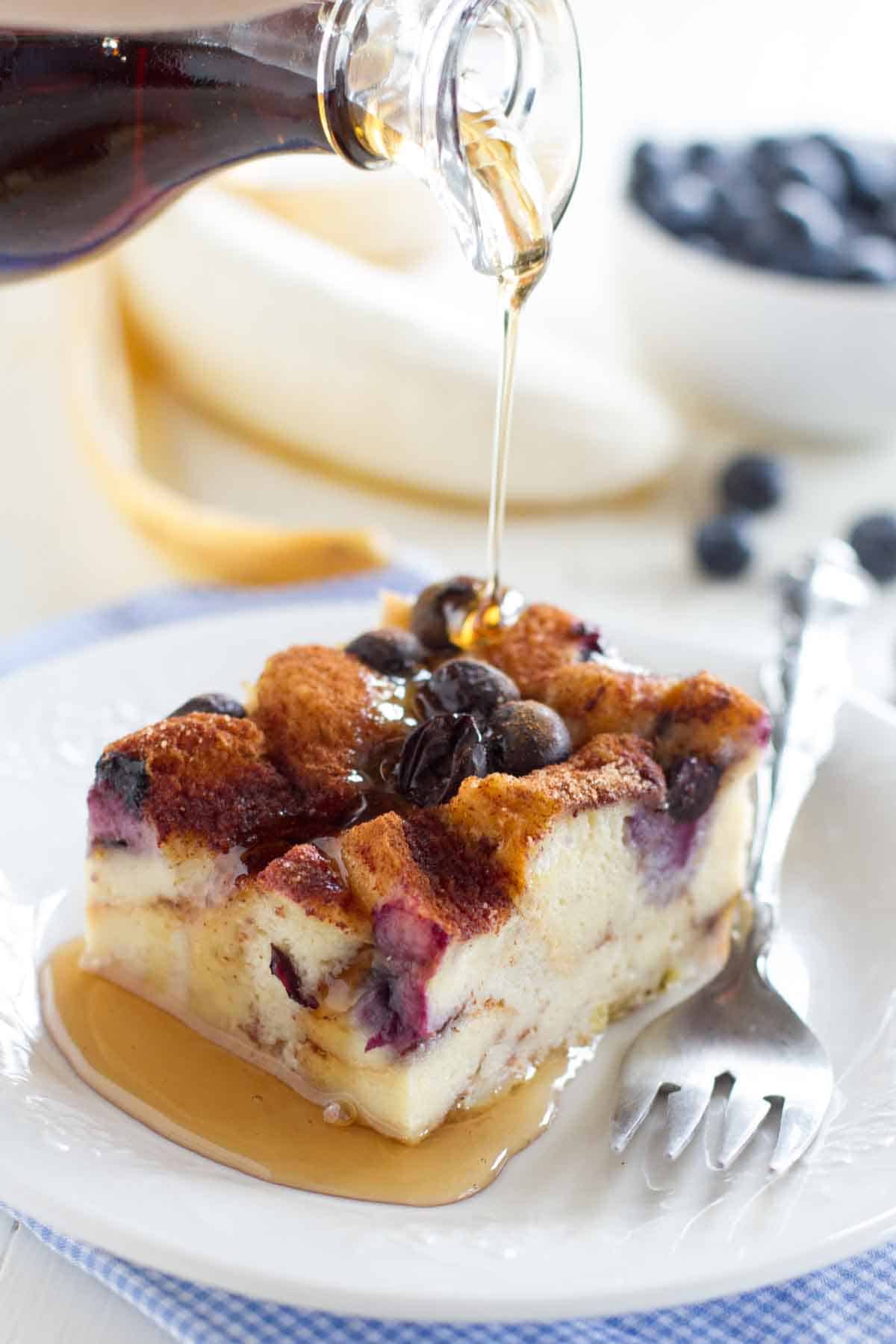 pouring syrup over a slice of blueberry banana french toast bake