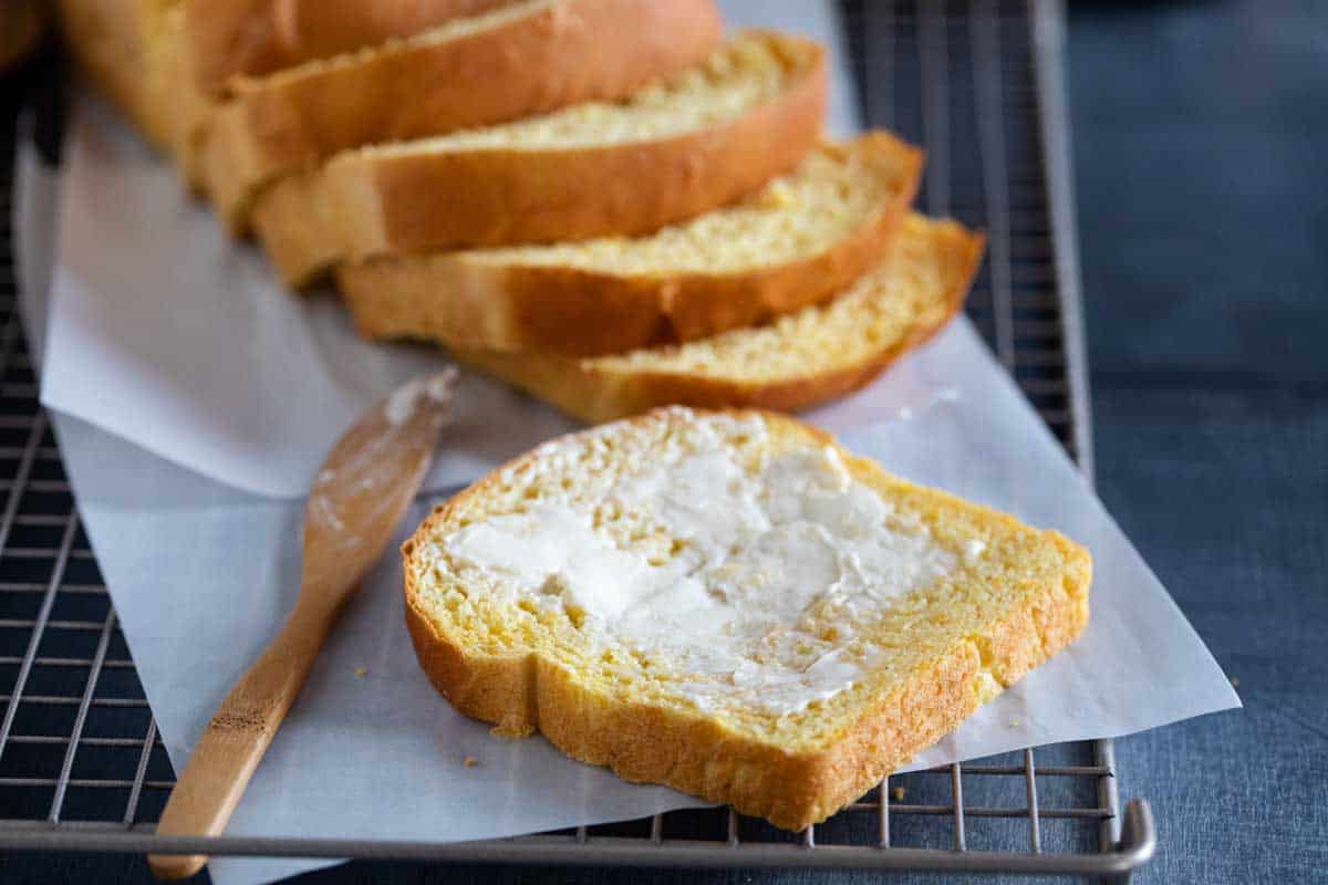 Slice of bread with butter in front of the loaf of bread.