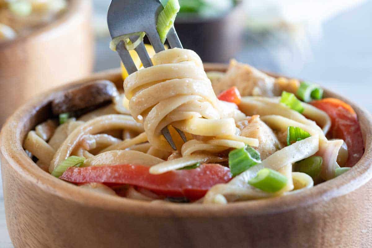 wooden bowl filled with Cajun Chicken Pasta with a fork grabbing the pasta.