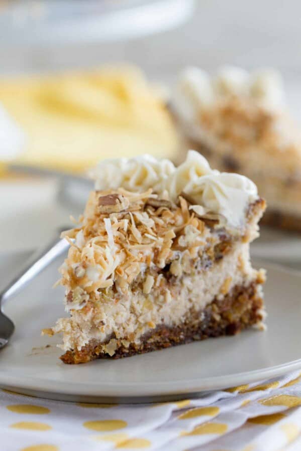 slice of carrot cake cheesecake topped with toasted coconut on a plate