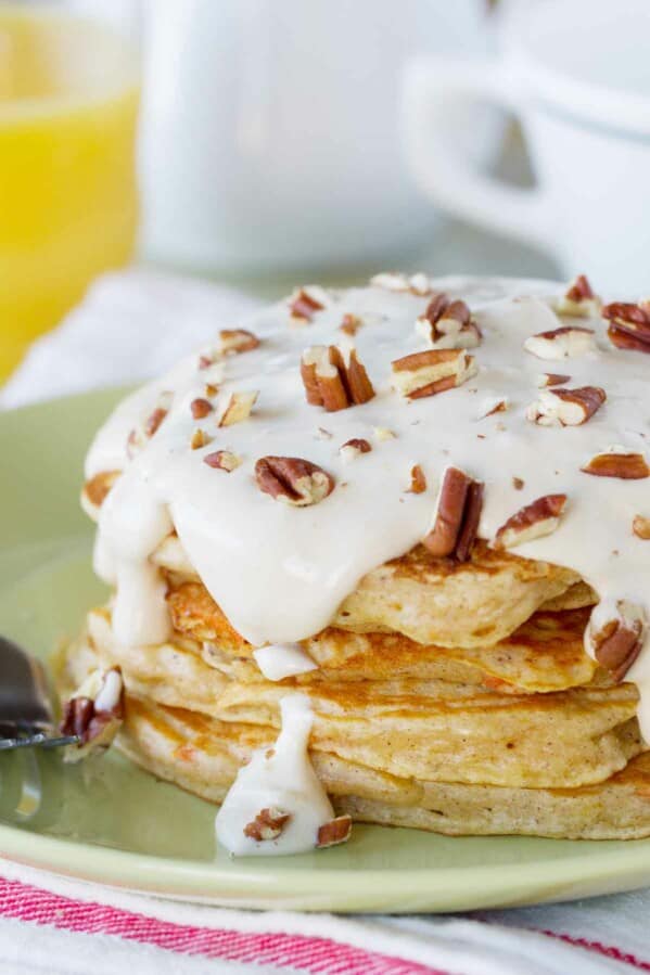 stack of carrot cake pancakes topped with maple cream cheese syrup and nuts.