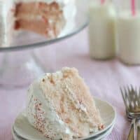 A slice of cherry chip cake with fluffy frosting on a stack of plates.