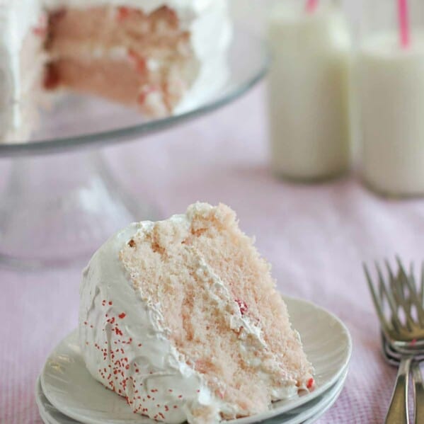 A slice of cherry chip cake with fluffy frosting on a stack of plates.