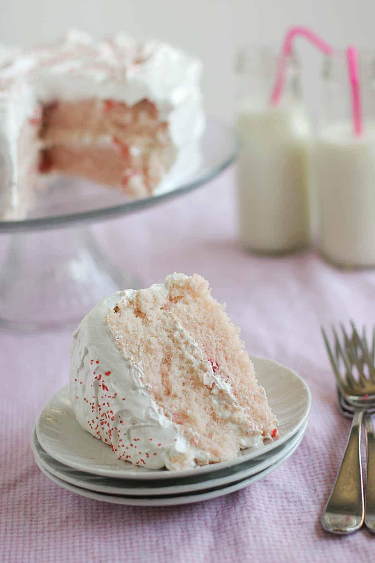 A slice of cherry chip cake with fluffy frosting on a stack of plates.