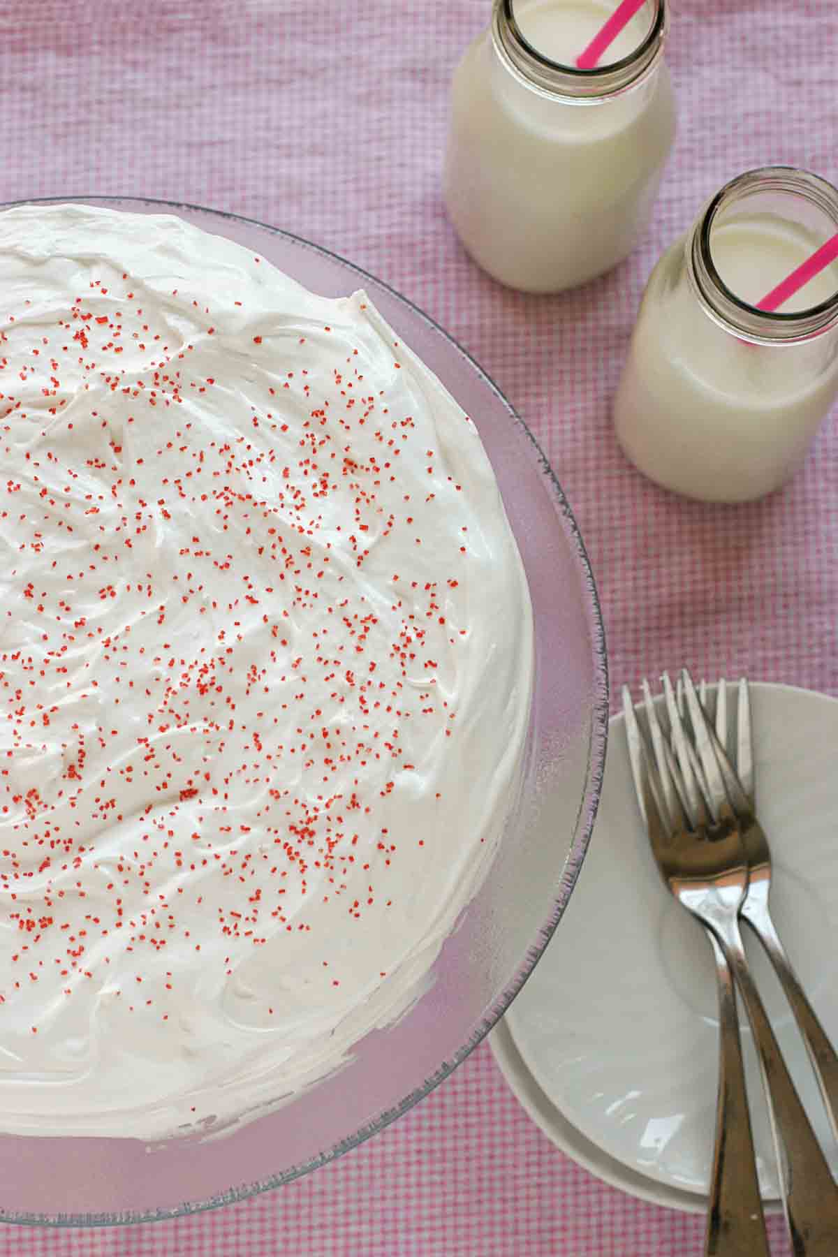 Overhead view of cherry chip cake with fluffy frosting with two glasses of milk.