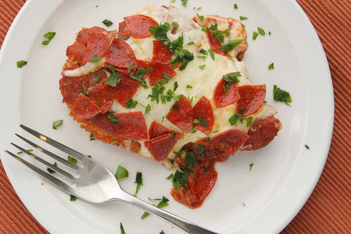 overhead view of chicken parmesan with pepperoni on a plate with a fork