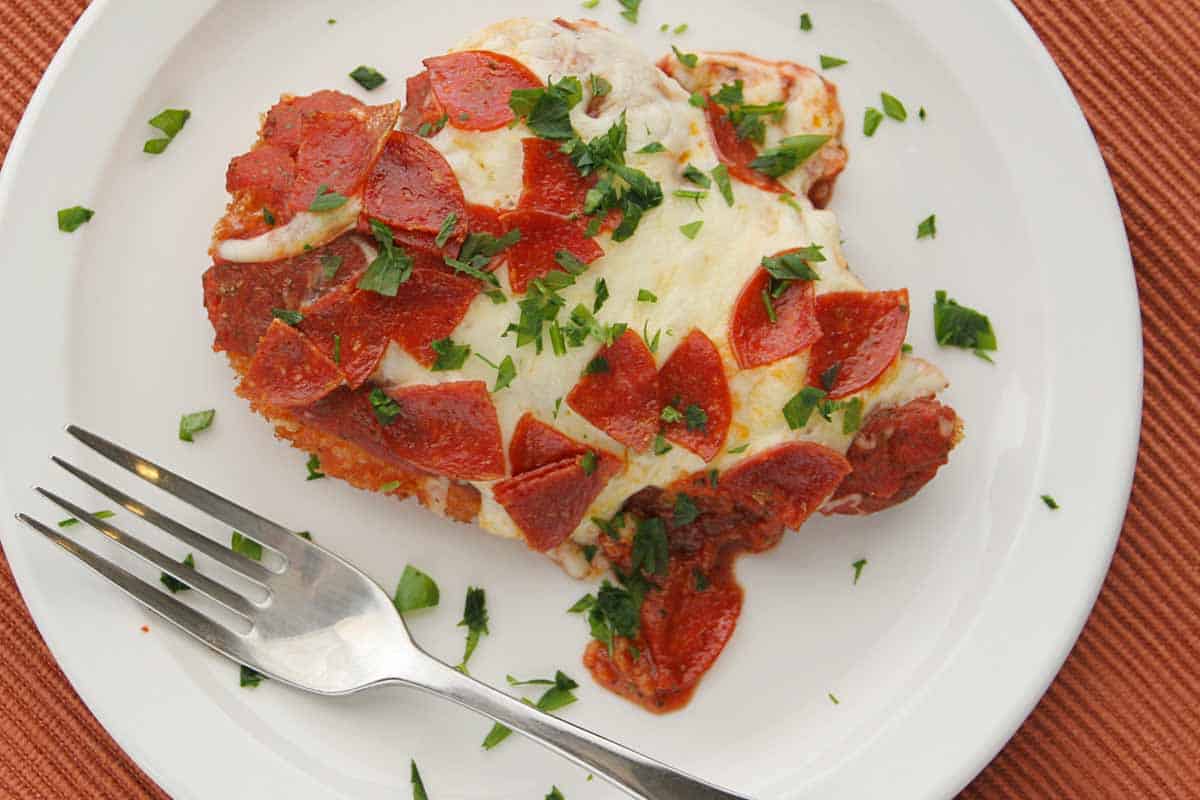 Chicken parmesan with a twist – chicken parmesan is topped with pepperoni for an exciting and different twist to a classic. overhead view of chicken parmesan with pepperoni on a plate with a fork