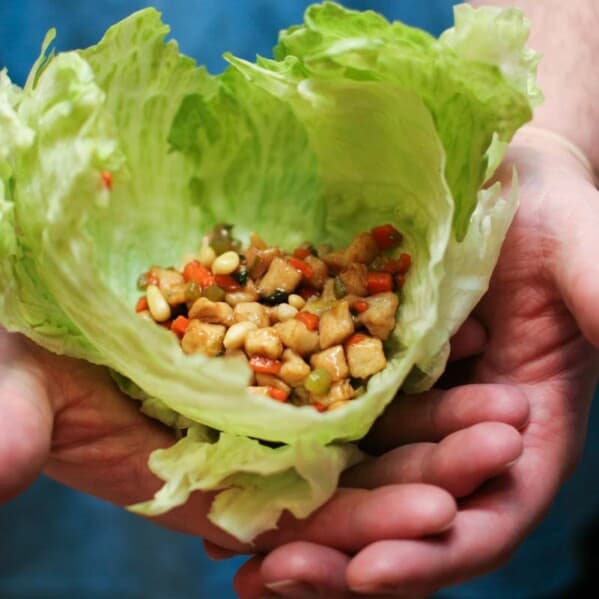 Chicken Soong filling inside of lettuce leaves being held by two hands.