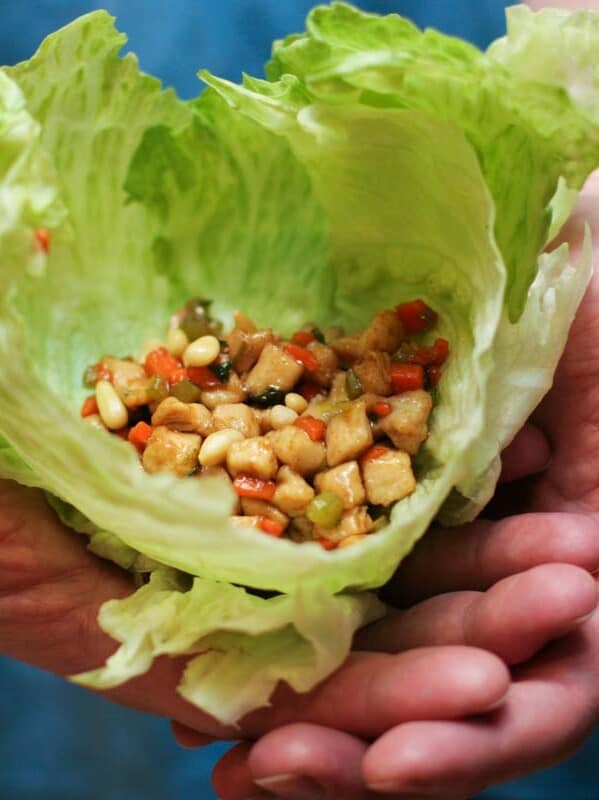 Chicken Soong filling inside of lettuce leaves being held by two hands.