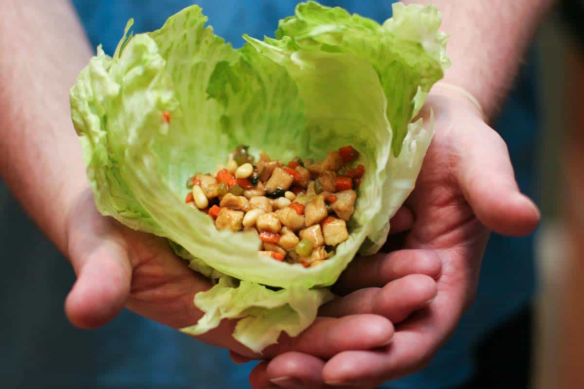 Chicken Soong filling inside of lettuce leaves being held by two hands.