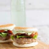 Two Club Burger Sliders with Avocado-Ranch Dressing on a cutting board with drink in the back