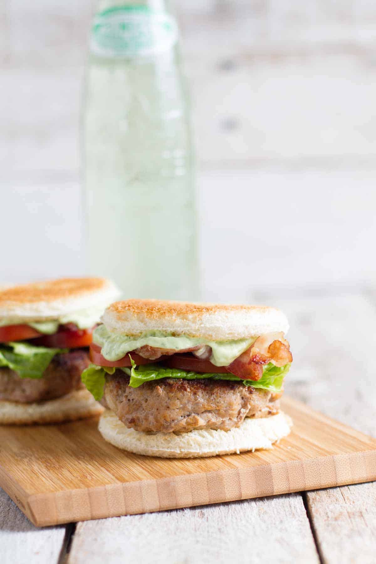 Two Club Burger Sliders with Avocado-Ranch Dressing on a cutting board with drink in the back