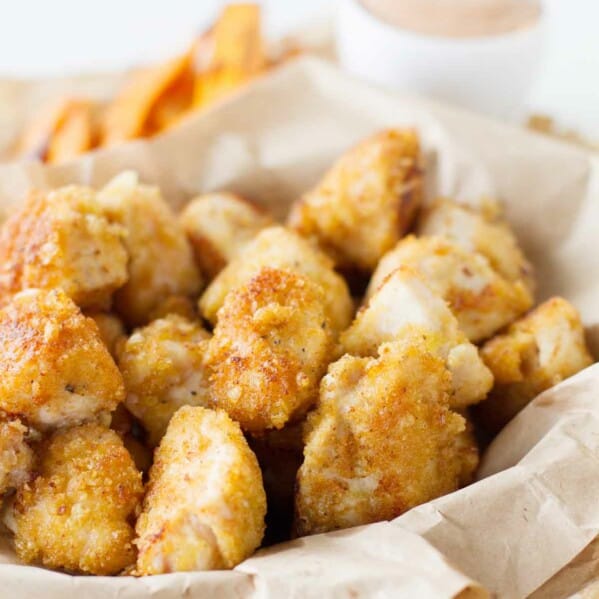 Crispy Chicken Nuggets in a basket with dipping sauce behind.