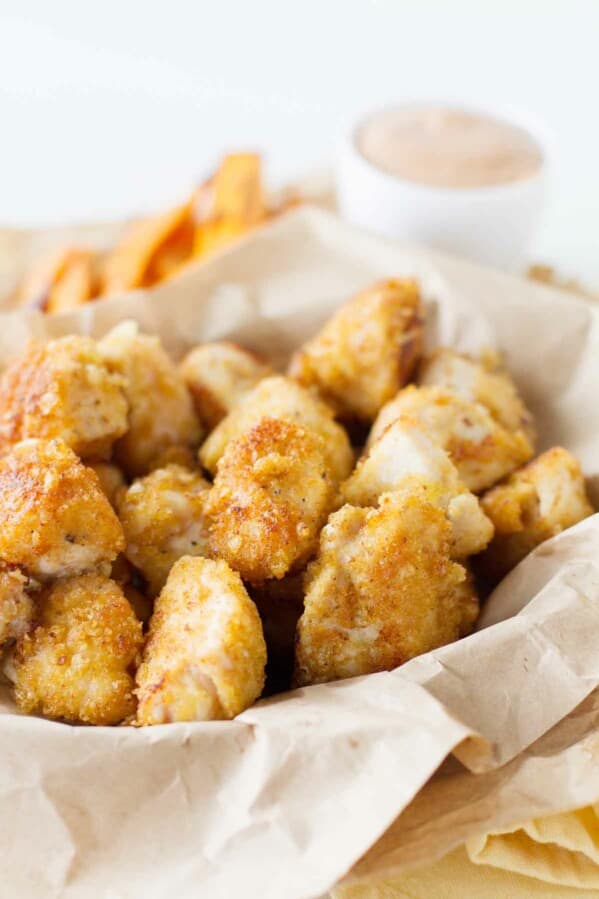 Crispy Chicken Nuggets in a basket with dipping sauce behind.