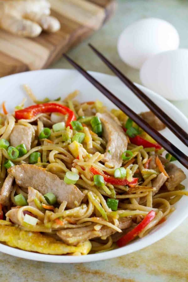 shallow bowl with egg and pork lo mein with chopsticks