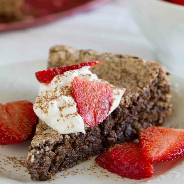 slice of Italian Chocolate Almond Flourless Cake topped with whipped cream and strawberries.