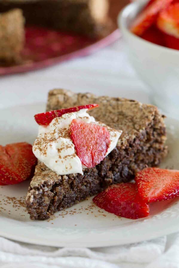 slice of Italian Chocolate Almond Flourless Cake topped with whipped cream and strawberries.