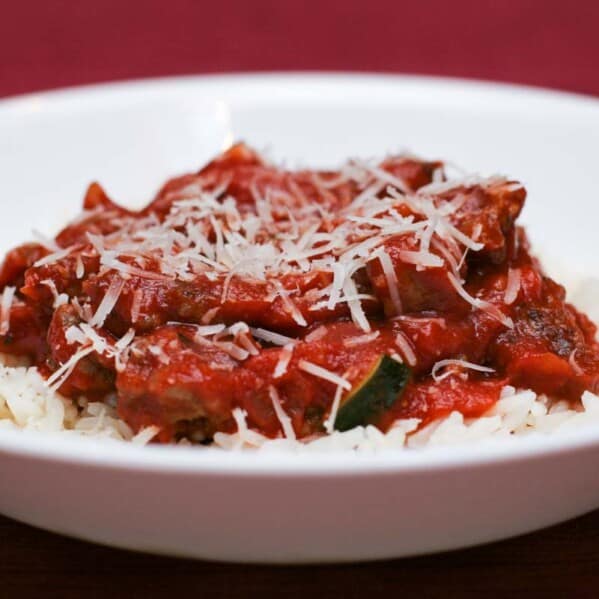 Italian Sausage and Red Sauce with Rice in a shallow bowl with a red background