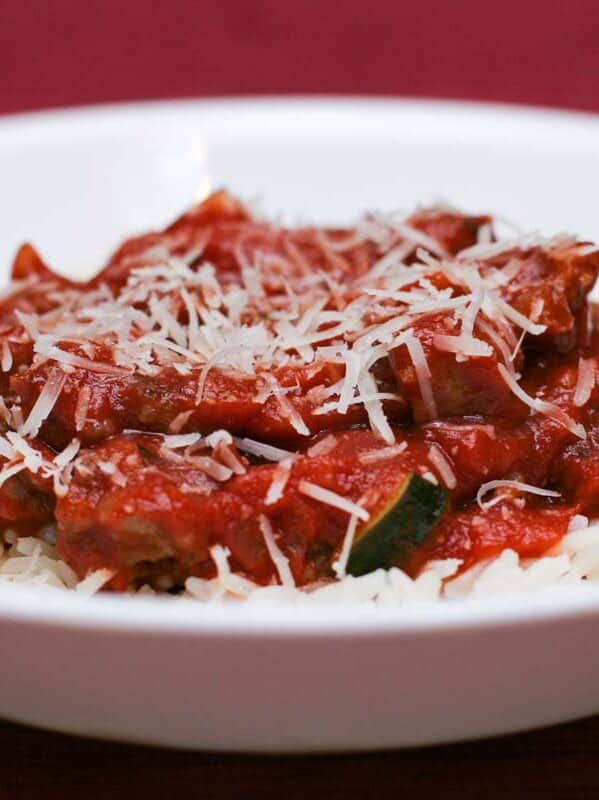 Italian Sausage and Red Sauce with Rice in a shallow bowl with a red background