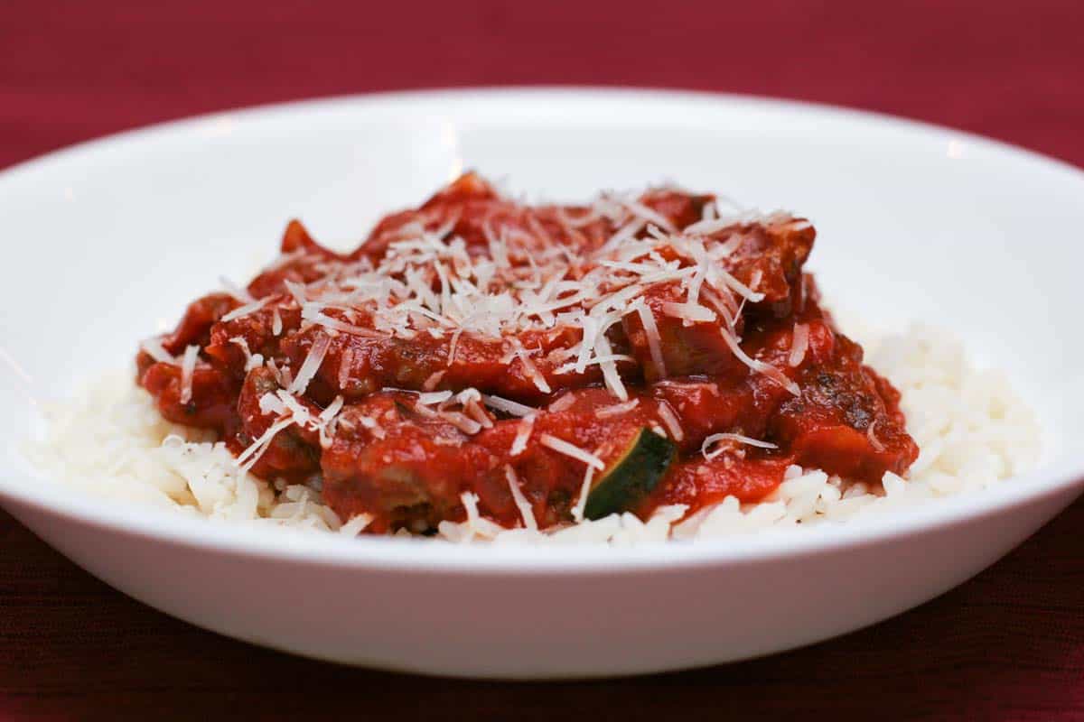 Italian Sausage and Red Sauce with Rice in a shallow bowl with a red background