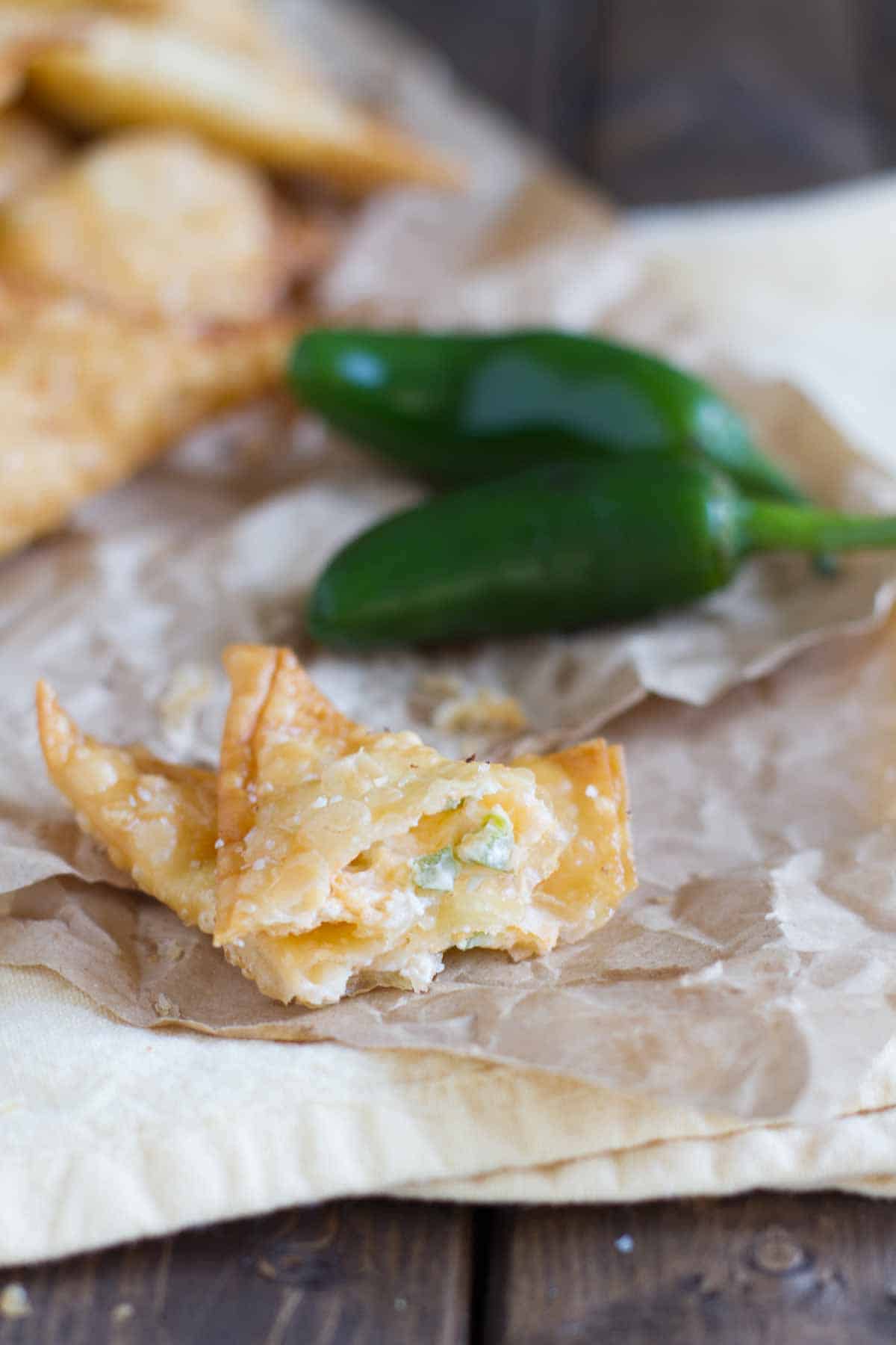 These Jalapeno Popper Wontons are fried wontons that are stuffed with cream cheese and jalapeños in this tasty appetizer. Jalapeno Popper Wonton on paper opened up to show filling.