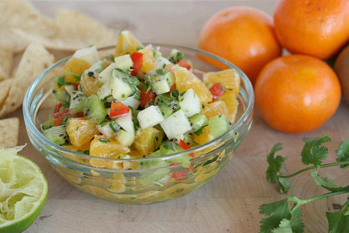 Kiwi and Tangerine Salsa in a bowl with oranges and limes on the side
