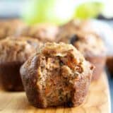 Morning glory muffin on a wooden board with a bite taken from it to show texture.