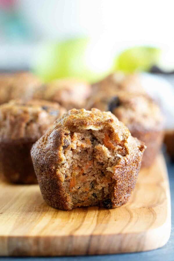 Morning glory muffin on a wooden board with a bite taken from it to show texture.