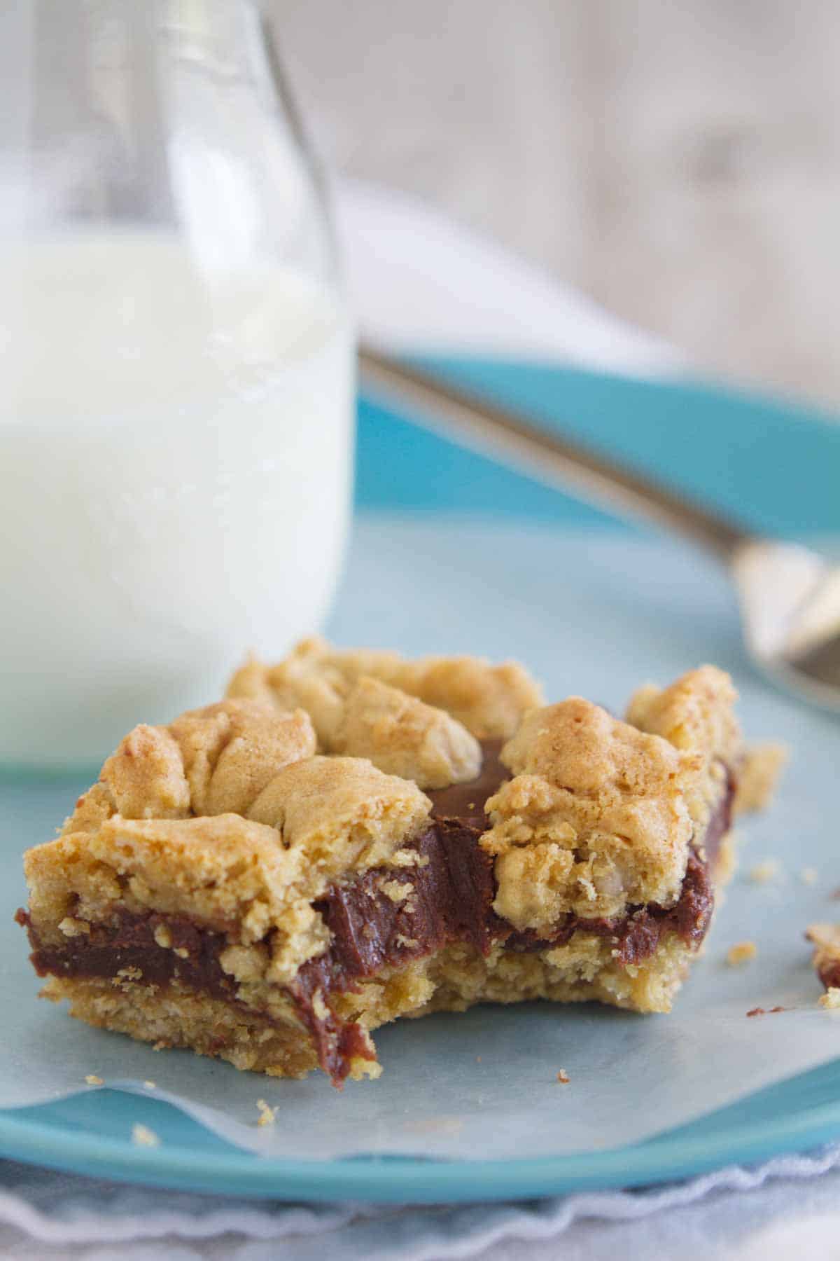 Gooey chocolate is sandwiched between two layers of oatmeal cookies in these decadent Oatmeal Fudge Bars. Oatmeal fudge bar on a blue plate with a bite taken from it.