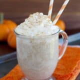 Warm pumpkin drink in a clear mug topped with whipped cream.