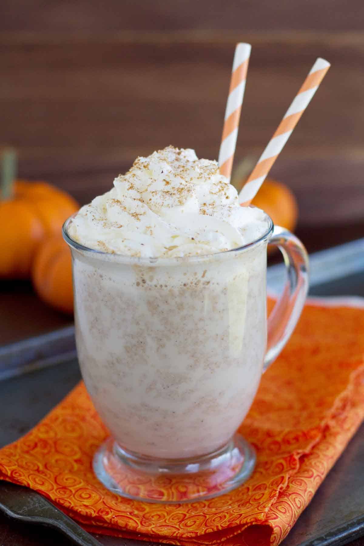 Warm pumpkin drink in a clear mug topped with whipped cream.