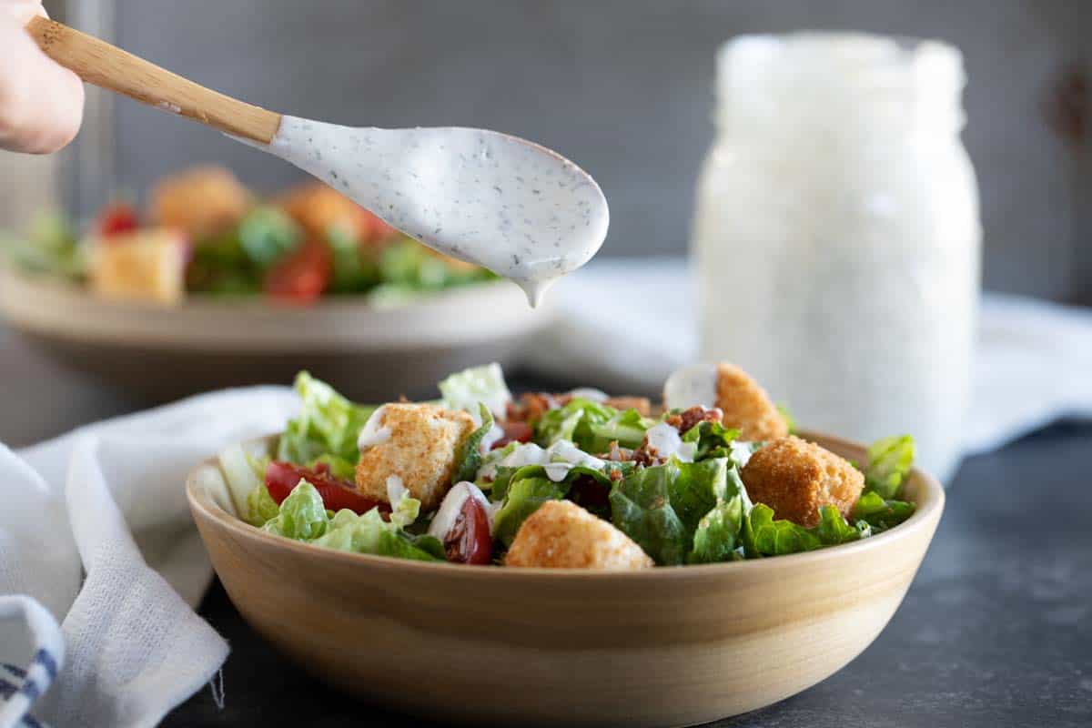 spooning homemade ranch over a salad in a bowl