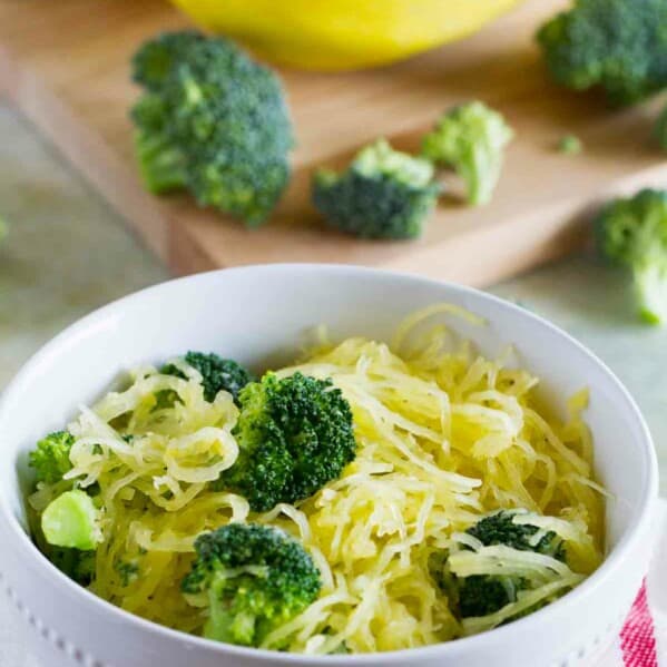 bowl filled with spaghetti squash with broccoli with more veggies on a cutting board behind.