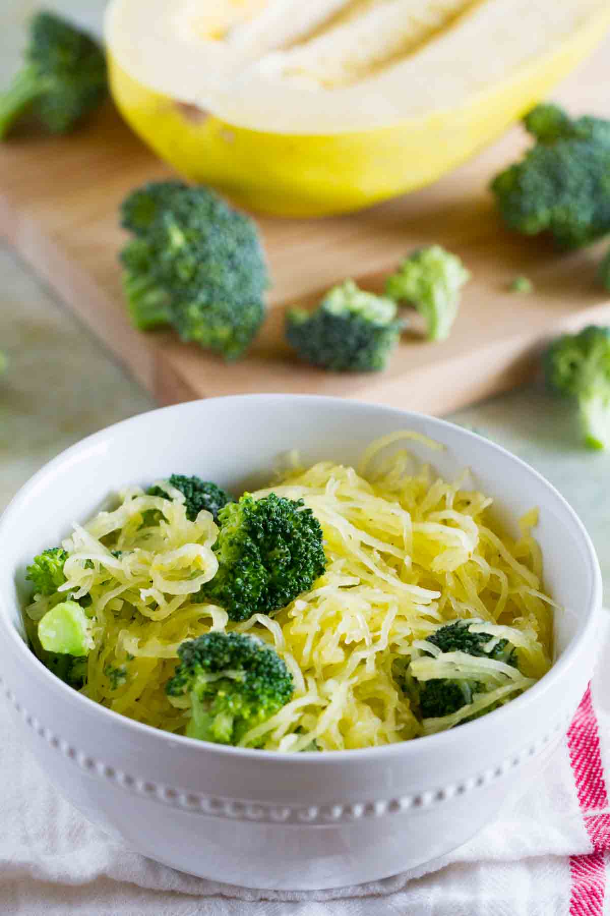 bowl filled with spaghetti squash with broccoli with more veggies on a cutting board behind.
