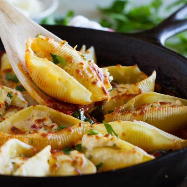 spooning out a shell from a pan full of stuffed pasta shells