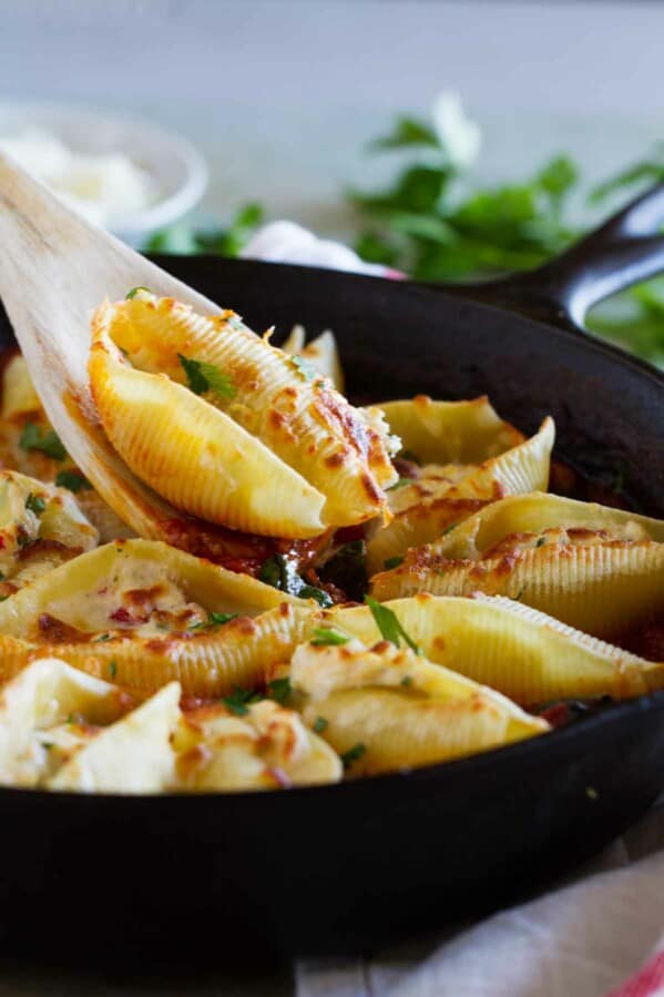 spooning out a shell from a pan full of stuffed pasta shells