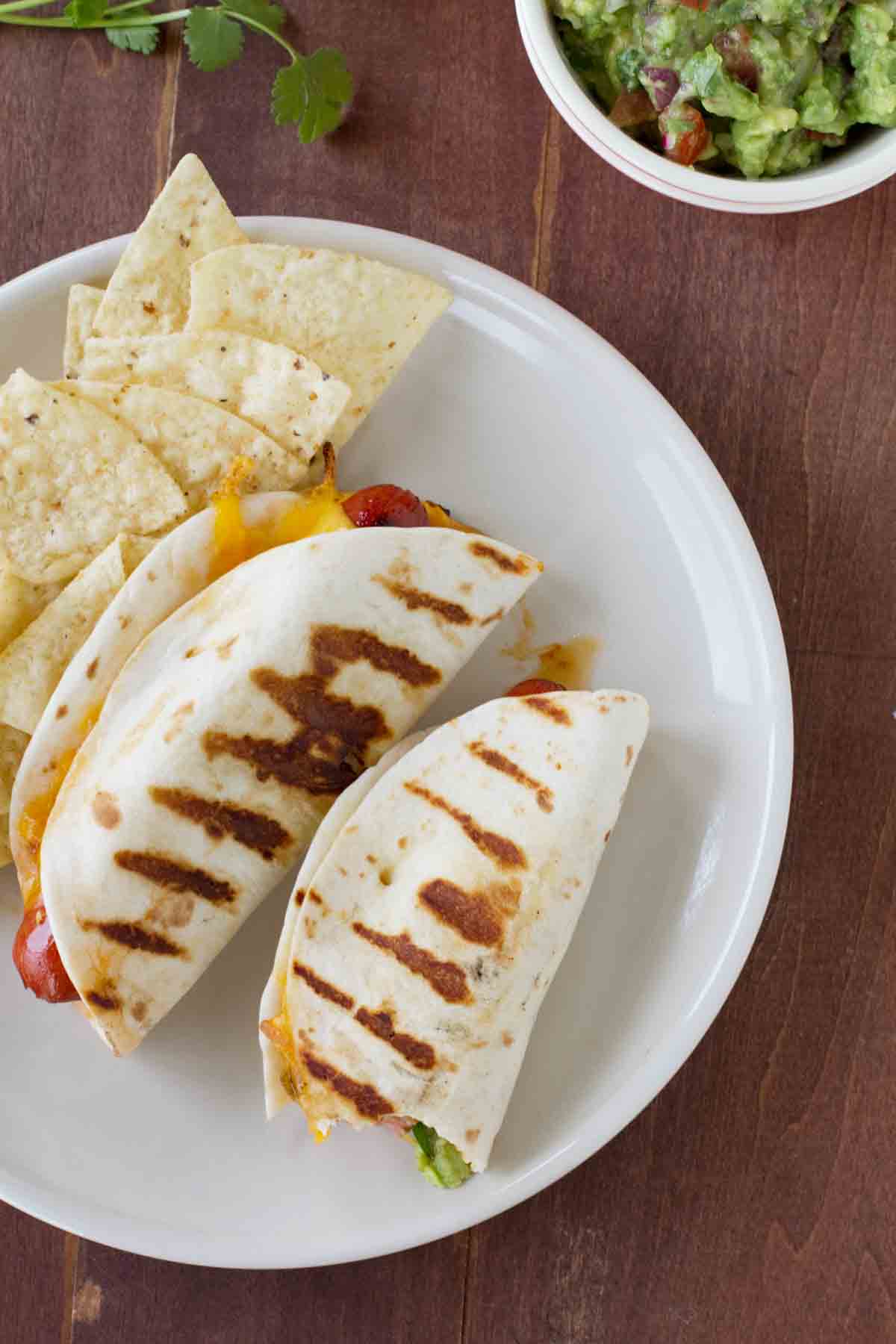 overhead view of two taco hot dogs on a plate with tortilla chips