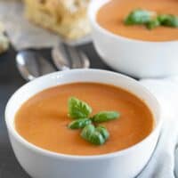 two bowls of tomato basil soup topped with fresh basil.