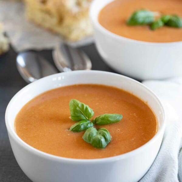 two bowls of tomato basil soup topped with fresh basil.