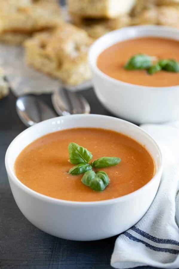 two bowls of tomato basil soup topped with fresh basil.