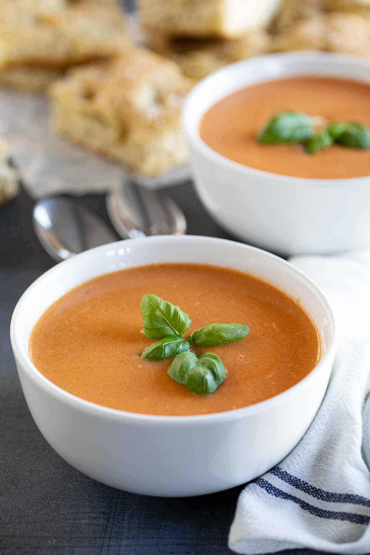 two bowls of tomato basil soup topped with fresh basil.