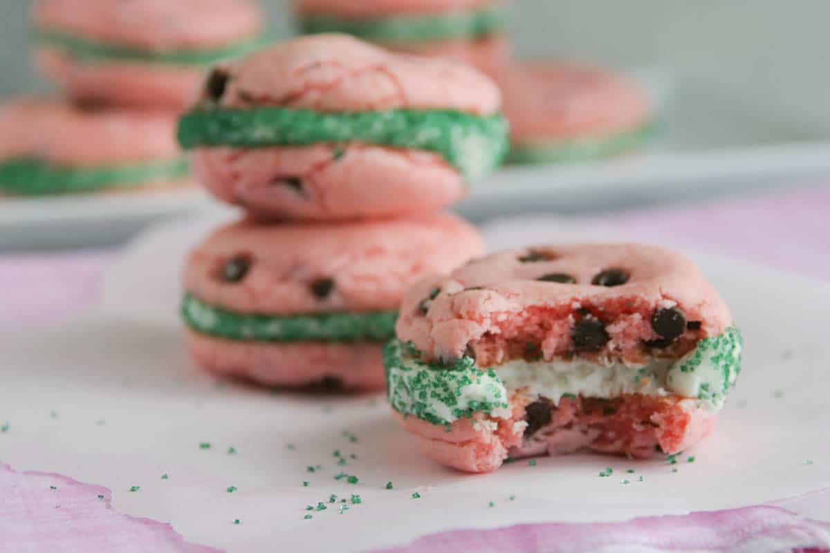 watermelon cake mix cookie sandwich with a bite taken from it with cookies stacked behind