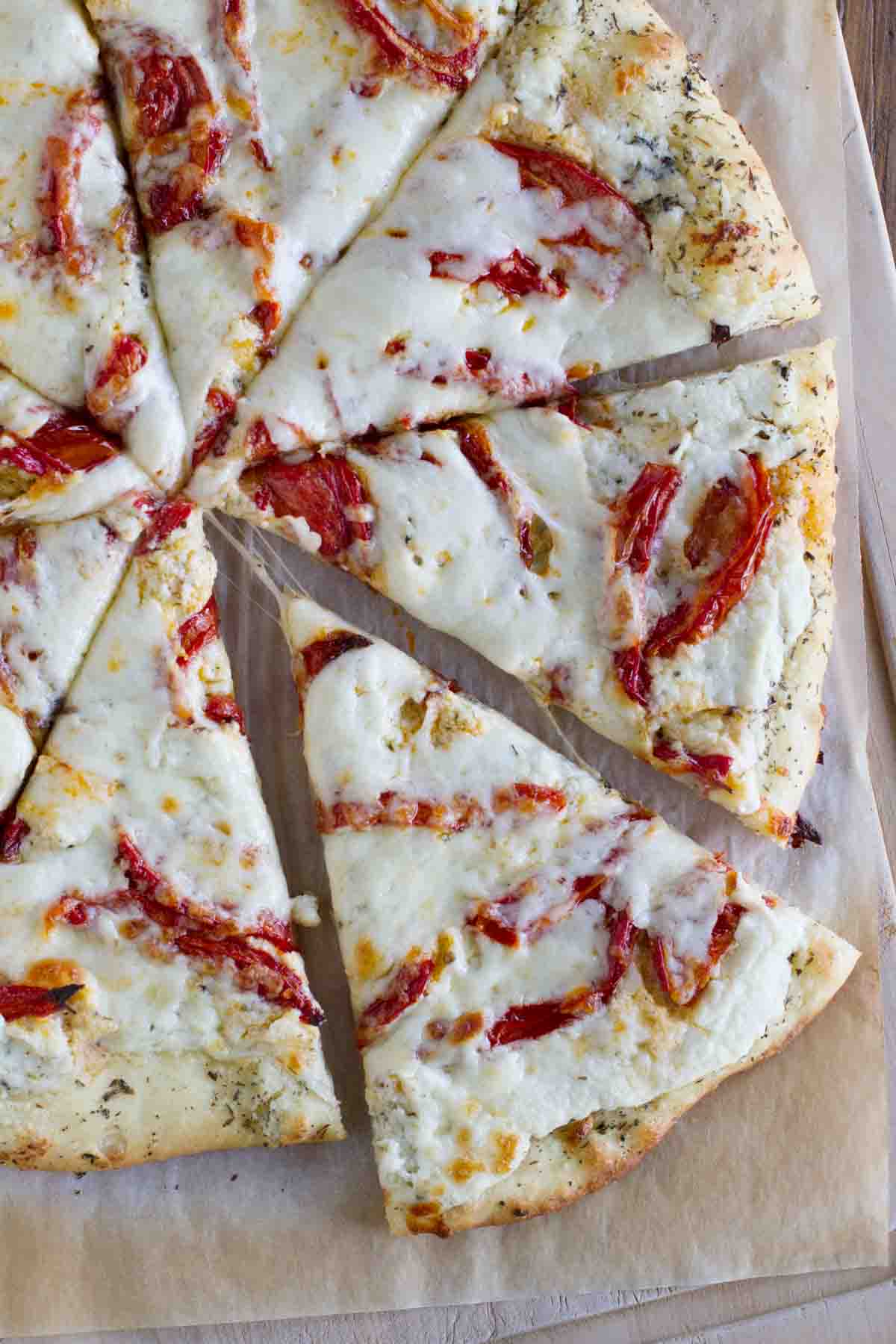 overhead view of a white pizza with roasted tomatoes cut into slices