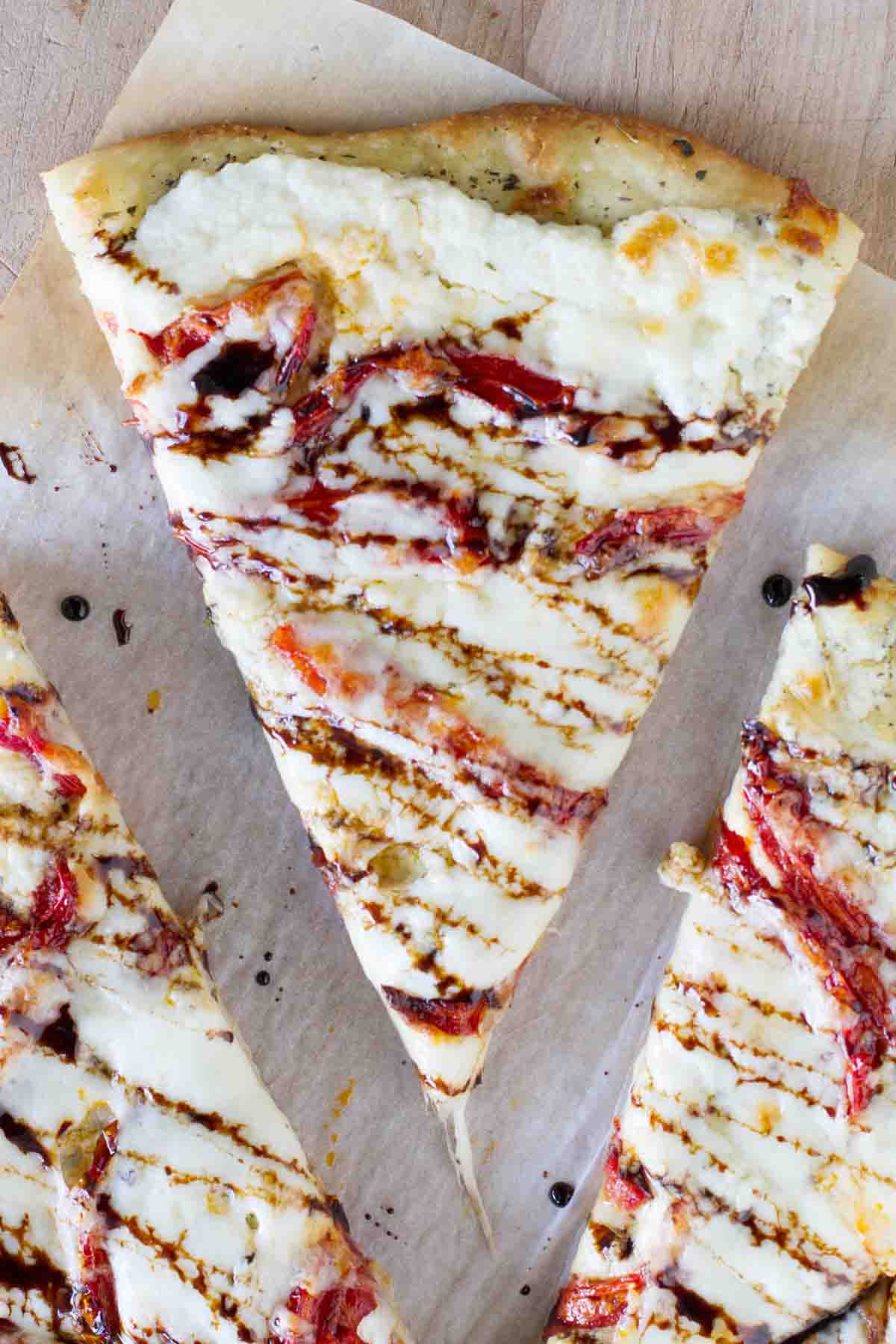 overhead view of a single slice of white pizza with roasted tomatoes, drizzled with balsamic