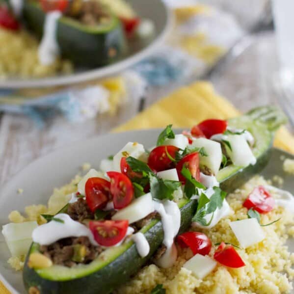 Zucchini boat topped with yogurt and tomatoes on top of a bed of couscous